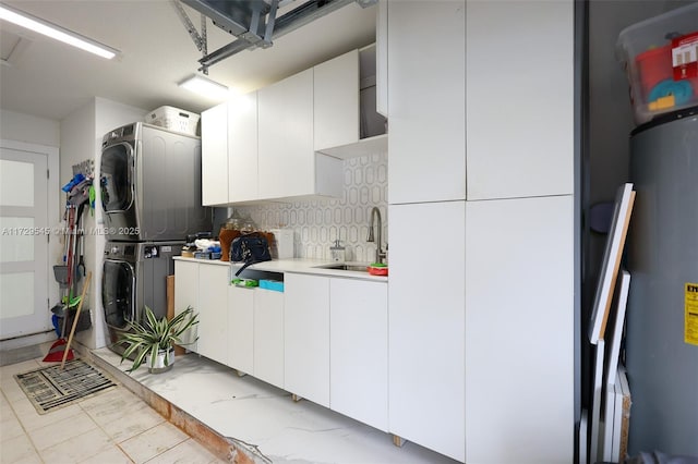 kitchen featuring tasteful backsplash, white cabinets, light countertops, stacked washing maching and dryer, and a sink