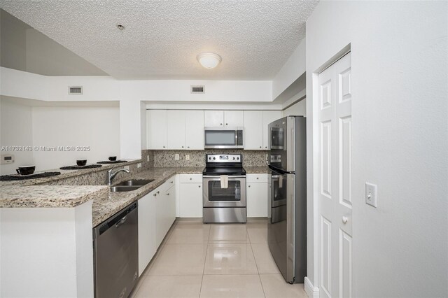 kitchen with sink, light tile patterned floors, appliances with stainless steel finishes, white cabinetry, and light stone counters