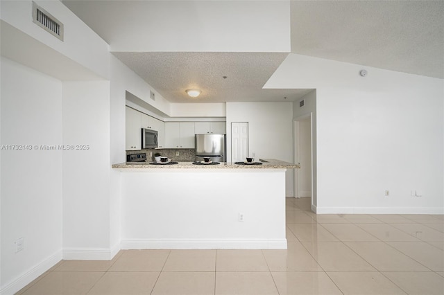 kitchen with tasteful backsplash, a textured ceiling, appliances with stainless steel finishes, kitchen peninsula, and white cabinets