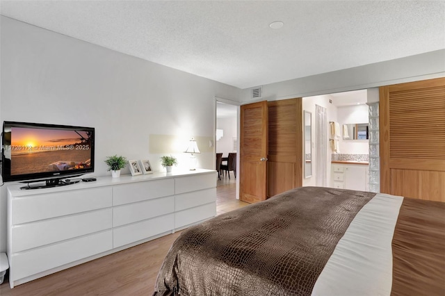 bedroom featuring connected bathroom, light hardwood / wood-style floors, and a textured ceiling