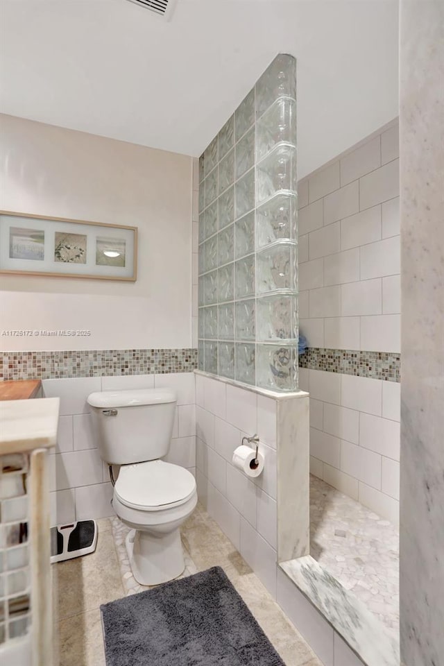 bathroom with tile walls, tile patterned flooring, toilet, and a shower