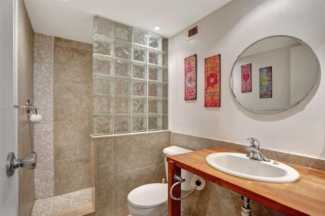 bathroom featuring toilet, sink, tile walls, and a tile shower