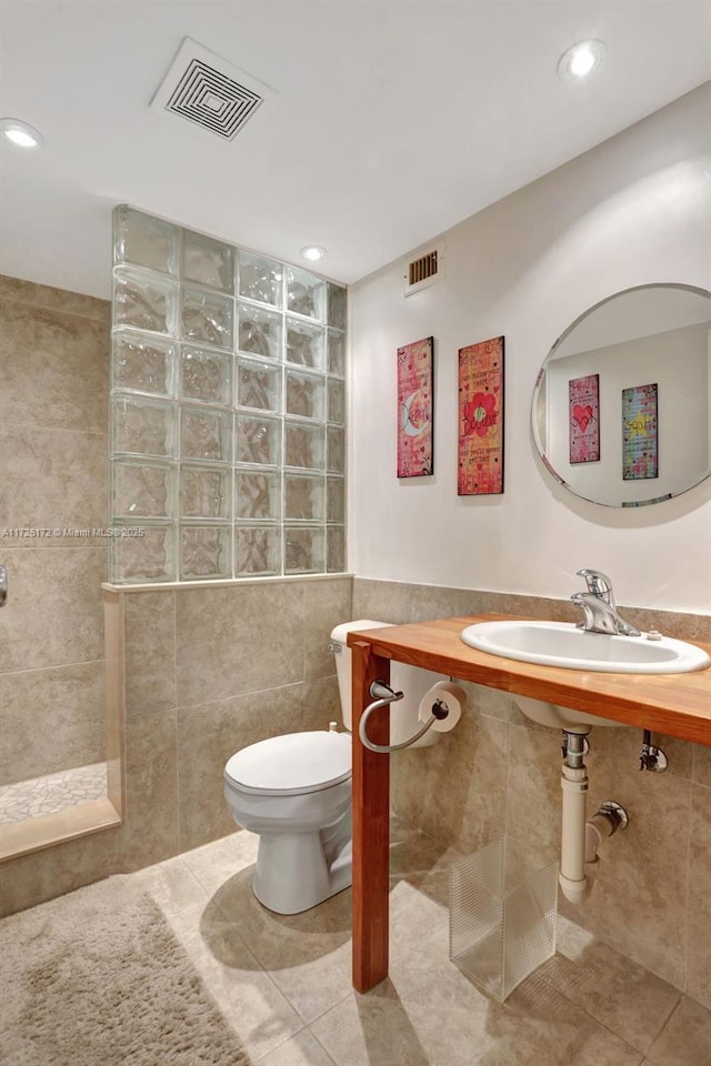 bathroom with toilet, sink, tile walls, a tile shower, and tile patterned flooring