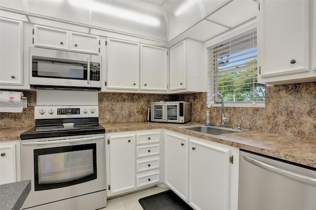 kitchen with light tile patterned flooring, appliances with stainless steel finishes, white cabinetry, sink, and backsplash