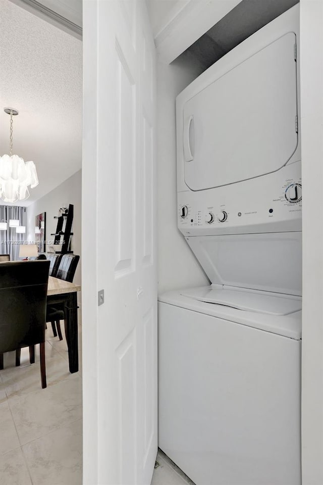 washroom with stacked washing maching and dryer and an inviting chandelier