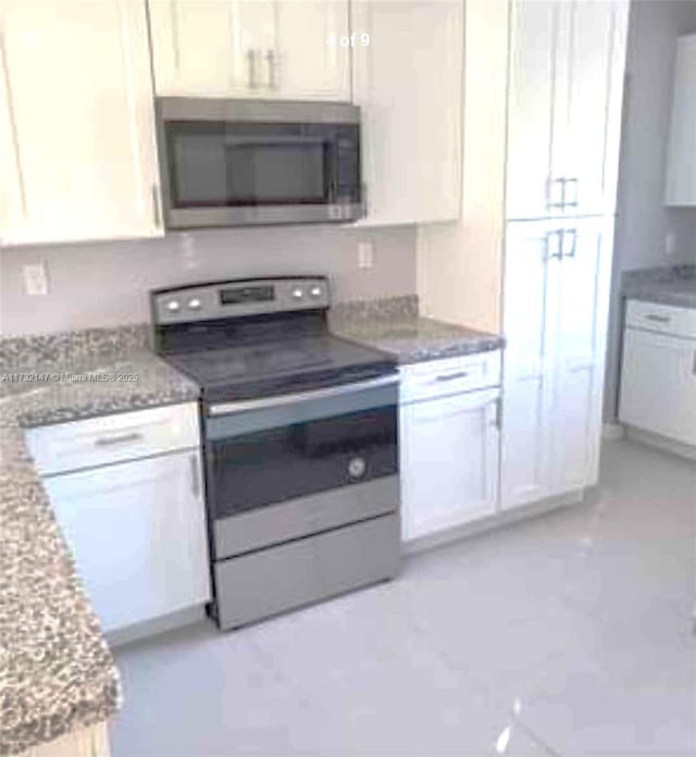 kitchen featuring stainless steel appliances, light stone counters, and white cabinetry