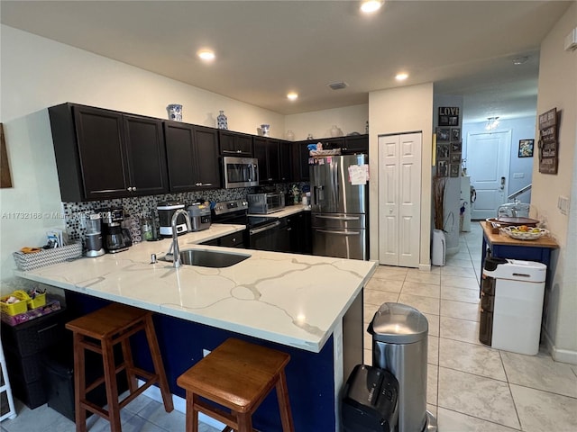 kitchen featuring sink, a kitchen breakfast bar, kitchen peninsula, stainless steel appliances, and light stone countertops