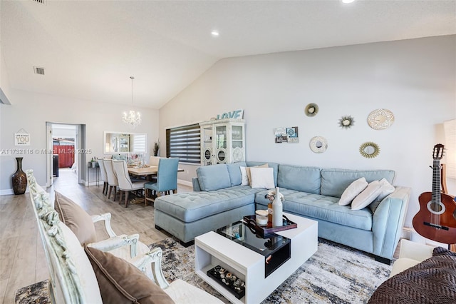 living room with a notable chandelier, vaulted ceiling, and light hardwood / wood-style floors