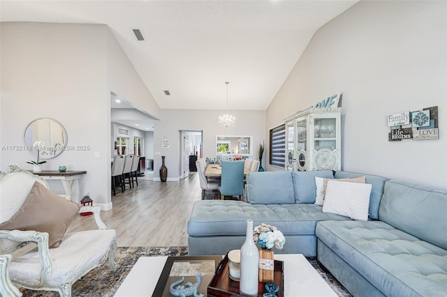 living room with high vaulted ceiling, a notable chandelier, and light hardwood / wood-style floors