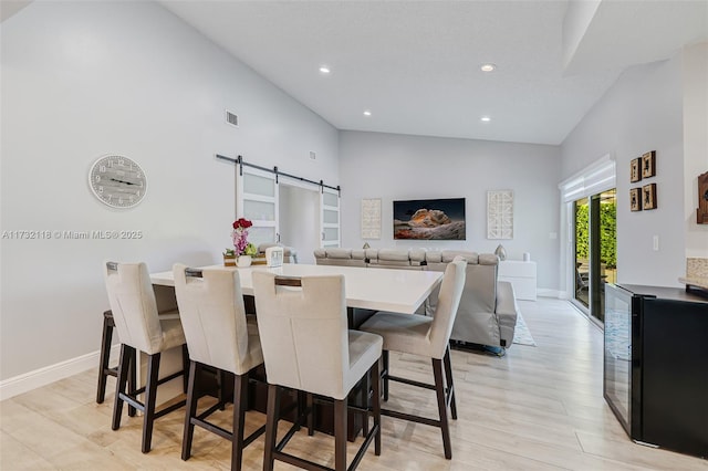 dining area featuring a barn door, high vaulted ceiling, and light hardwood / wood-style flooring