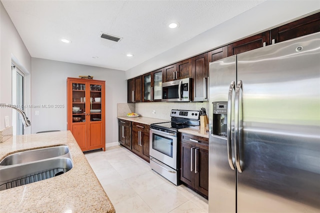 kitchen with light stone counters, stainless steel appliances, sink, and tasteful backsplash