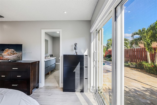 bedroom featuring connected bathroom, light hardwood / wood-style floors, and a textured ceiling