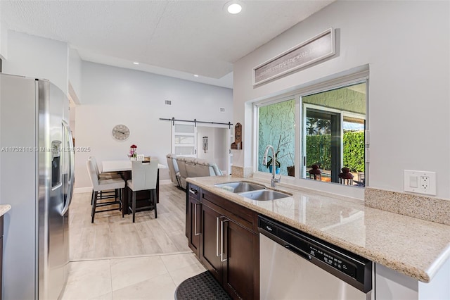 kitchen with light tile patterned flooring, appliances with stainless steel finishes, sink, light stone counters, and a barn door