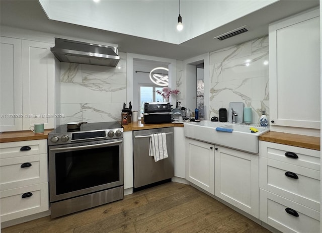 kitchen featuring white cabinetry, stainless steel appliances, butcher block counters, and wall chimney exhaust hood