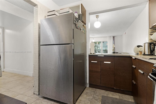 kitchen featuring stainless steel refrigerator, light tile patterned flooring, dark brown cabinets, and pendant lighting