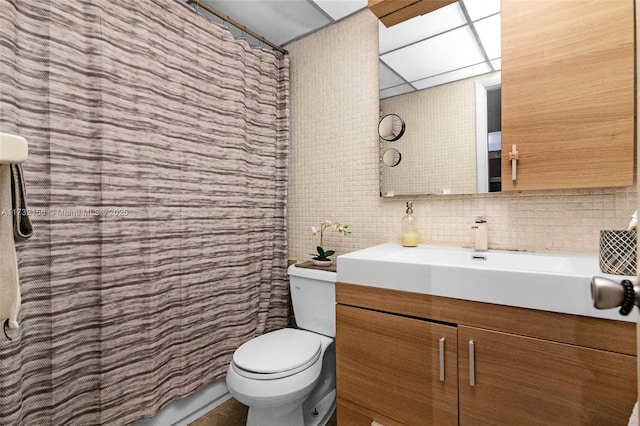 bathroom featuring vanity, a drop ceiling, backsplash, and toilet