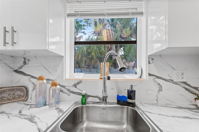 interior details with white cabinetry, light stone counters, sink, and decorative backsplash