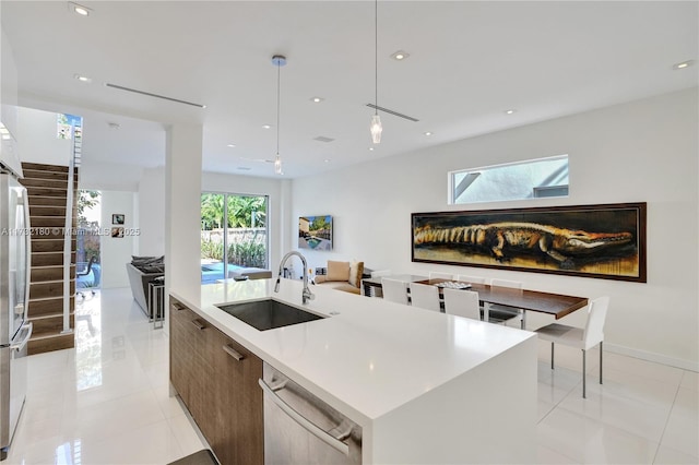 kitchen with sink, light tile patterned floors, stainless steel dishwasher, an island with sink, and pendant lighting