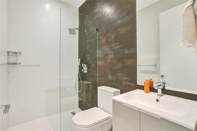 bathroom with tiled shower, vanity, toilet, and tile walls