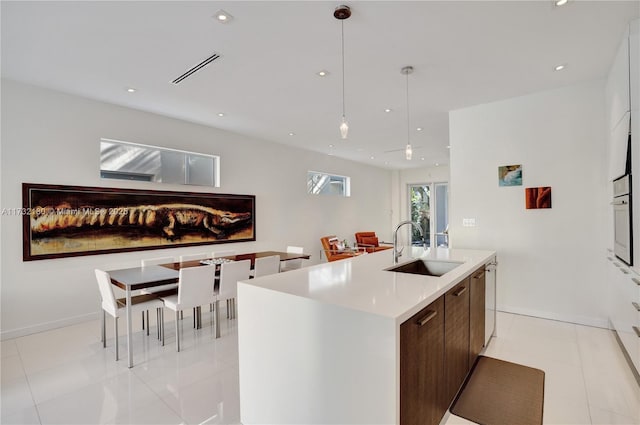 kitchen featuring a kitchen island with sink, sink, light tile patterned floors, and white cabinetry