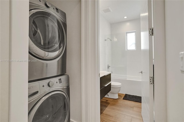 laundry room featuring stacked washing maching and dryer and light hardwood / wood-style flooring