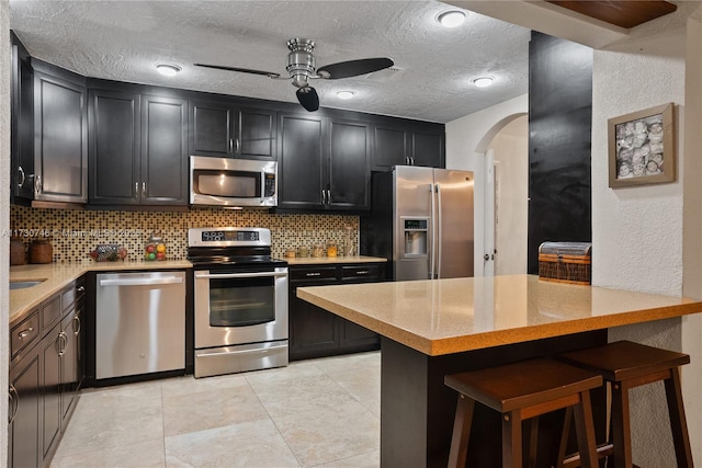 kitchen featuring tasteful backsplash, appliances with stainless steel finishes, a kitchen breakfast bar, and kitchen peninsula