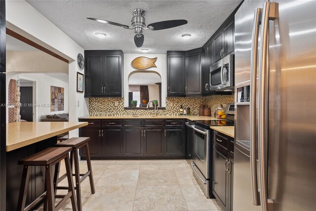 kitchen with sink, appliances with stainless steel finishes, a kitchen breakfast bar, tasteful backsplash, and a textured ceiling