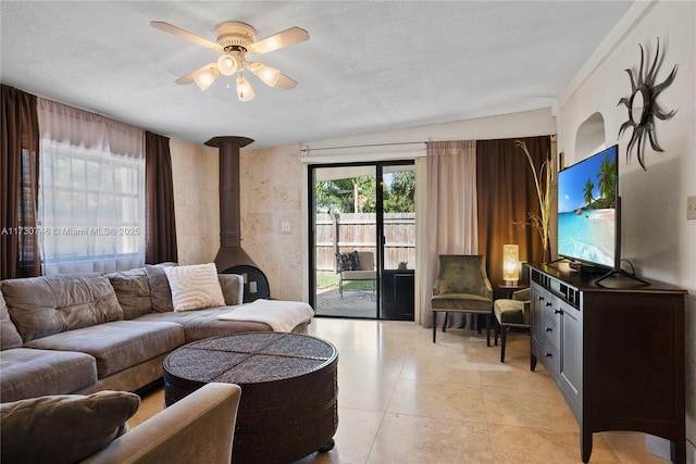 tiled living room featuring ceiling fan, a textured ceiling, and a wood stove