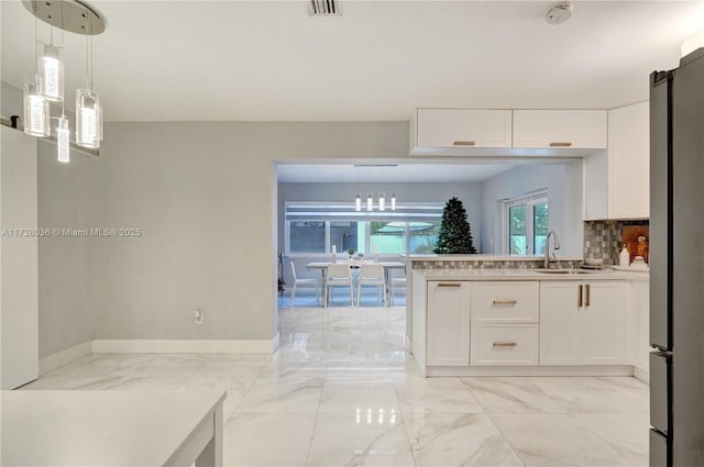 kitchen with sink, white cabinetry, stainless steel refrigerator, pendant lighting, and backsplash