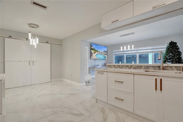 kitchen with white cabinetry, sink, decorative light fixtures, and a barn door