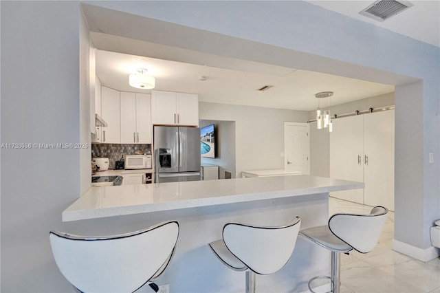 kitchen featuring stainless steel refrigerator with ice dispenser, kitchen peninsula, white cabinets, a barn door, and backsplash