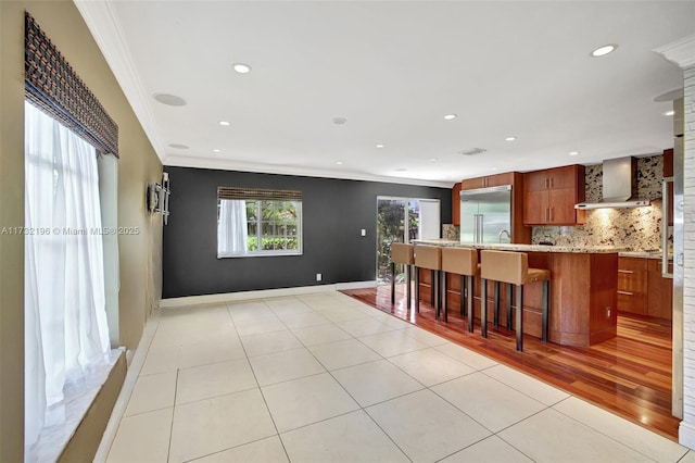 kitchen with a breakfast bar, ornamental molding, stainless steel built in fridge, decorative backsplash, and wall chimney exhaust hood