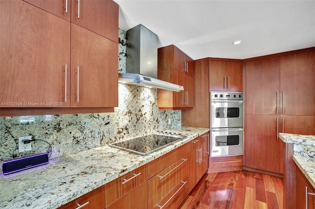 kitchen with tasteful backsplash, black electric cooktop, double oven, light hardwood / wood-style floors, and wall chimney range hood