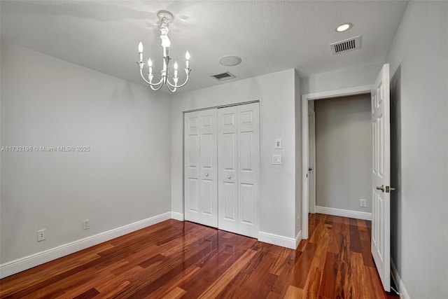 unfurnished bedroom featuring dark hardwood / wood-style floors, a textured ceiling, a closet, and a notable chandelier