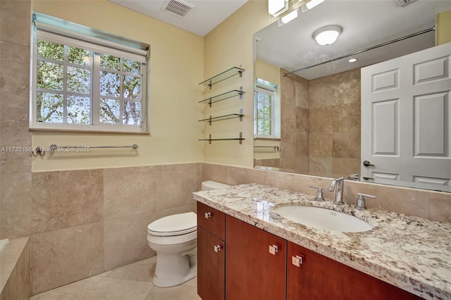 bathroom with a shower, tile walls, vanity, toilet, and tile patterned floors