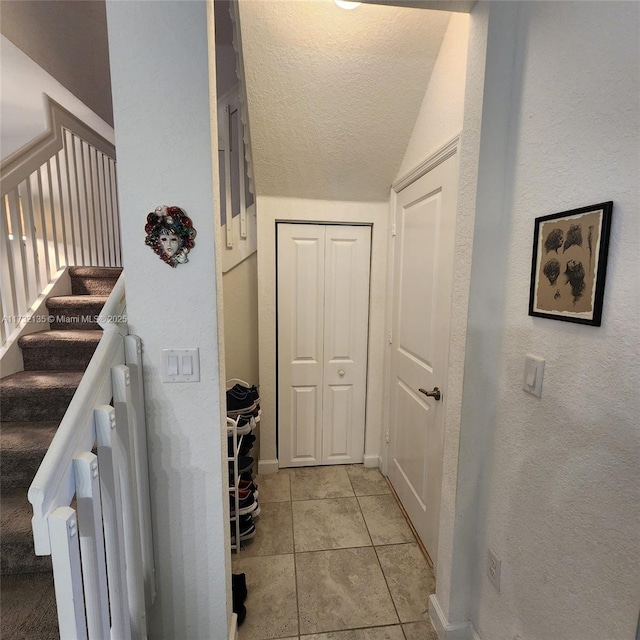 stairs with lofted ceiling, tile patterned flooring, and a textured ceiling