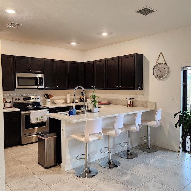 kitchen featuring light tile patterned floors, stainless steel appliances, a breakfast bar, and kitchen peninsula