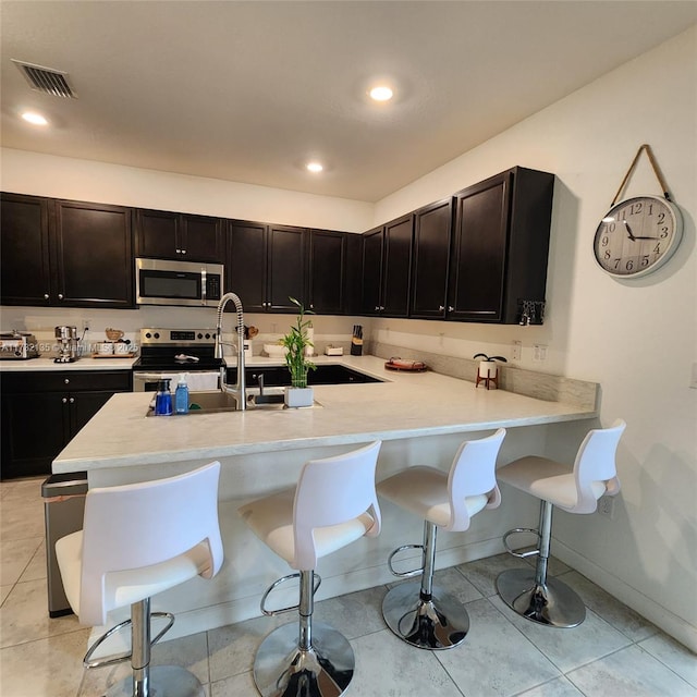 kitchen featuring light tile patterned flooring, a breakfast bar, sink, appliances with stainless steel finishes, and kitchen peninsula