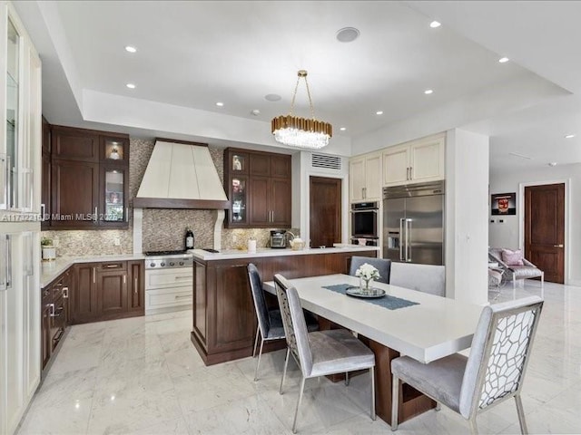 kitchen with premium range hood, stainless steel appliances, decorative backsplash, a kitchen island, and decorative light fixtures