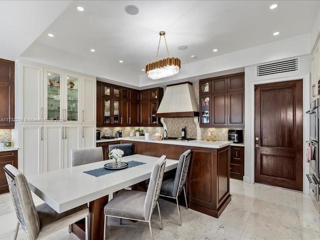 kitchen featuring a breakfast bar area, decorative backsplash, custom exhaust hood, hanging light fixtures, and a spacious island