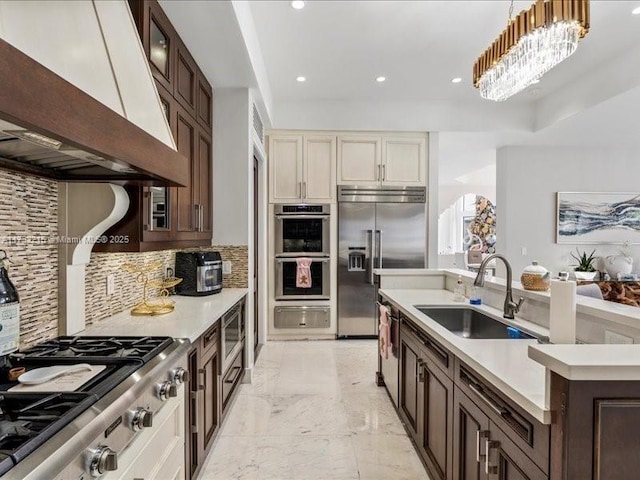 kitchen featuring pendant lighting, sink, built in appliances, tasteful backsplash, and custom range hood