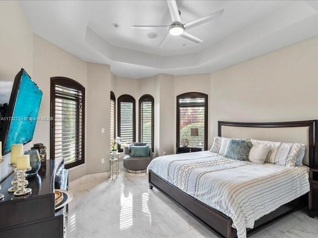 bedroom with multiple windows, a tray ceiling, and ceiling fan