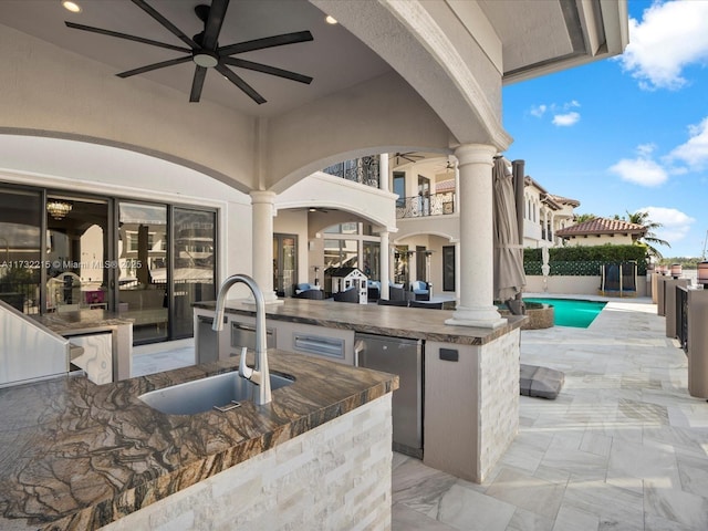 view of patio featuring exterior kitchen, ceiling fan, a fenced in pool, and sink