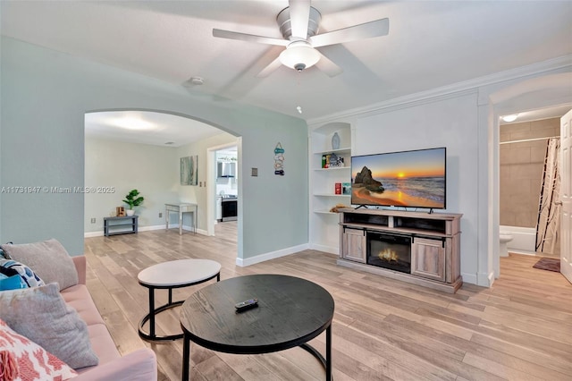 living room with ceiling fan, crown molding, light hardwood / wood-style floors, and built in shelves