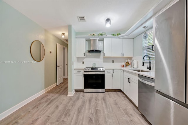 kitchen featuring white cabinetry, sink, stainless steel appliances, wall chimney range hood, and light hardwood / wood-style flooring