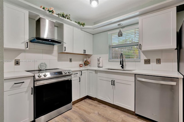 kitchen with sink, wall chimney range hood, stainless steel appliances, light hardwood / wood-style floors, and white cabinets