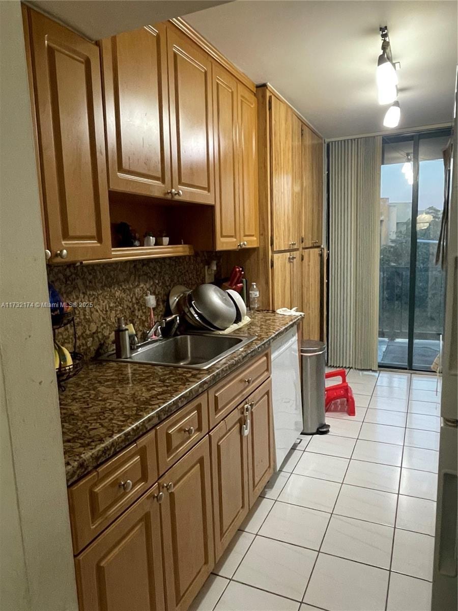 kitchen featuring sink, light tile patterned floors, white dishwasher, dark stone counters, and decorative backsplash