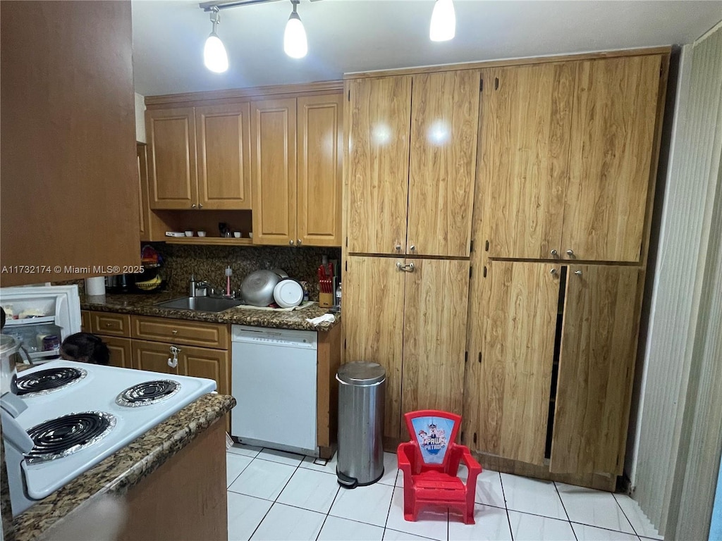 kitchen featuring sink, dark stone countertops, light tile patterned floors, white appliances, and backsplash