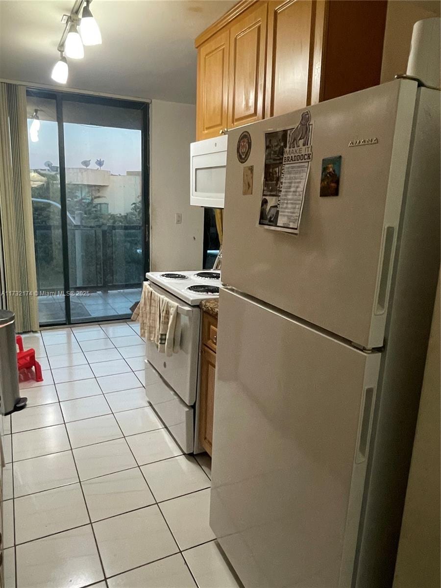 kitchen with light tile patterned flooring, white appliances, a wall of windows, and light brown cabinets