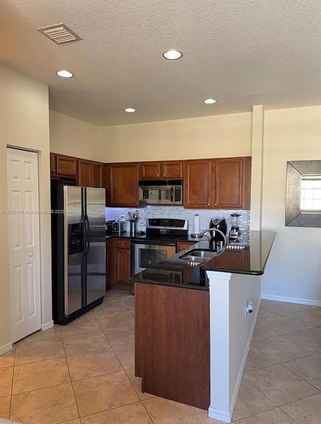 kitchen with light tile patterned floors, kitchen peninsula, a textured ceiling, and appliances with stainless steel finishes